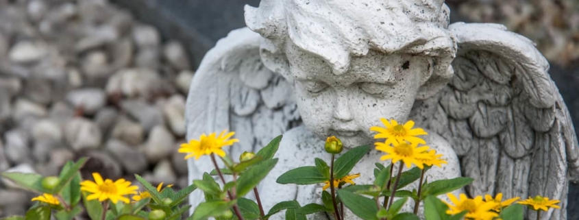 A stone cherub and yellow flowers decorate the grave of a wrongful death victim