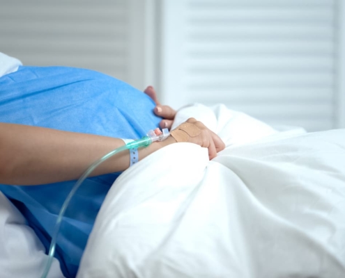 Pregnant woman hospitalized holds her stomach apprehensively.