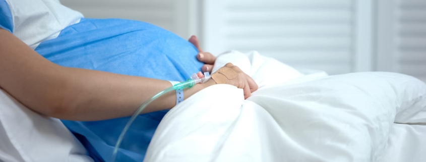 Pregnant woman hospitalized holds her stomach apprehensively.