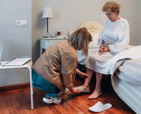 Caregiver putting slippers on an elderly person in an institution
