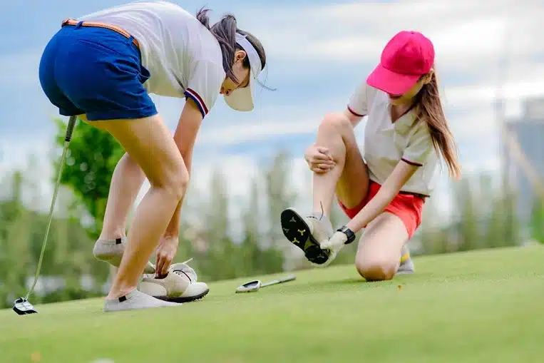 Two women taking their shoes off after suffering golf course injuries