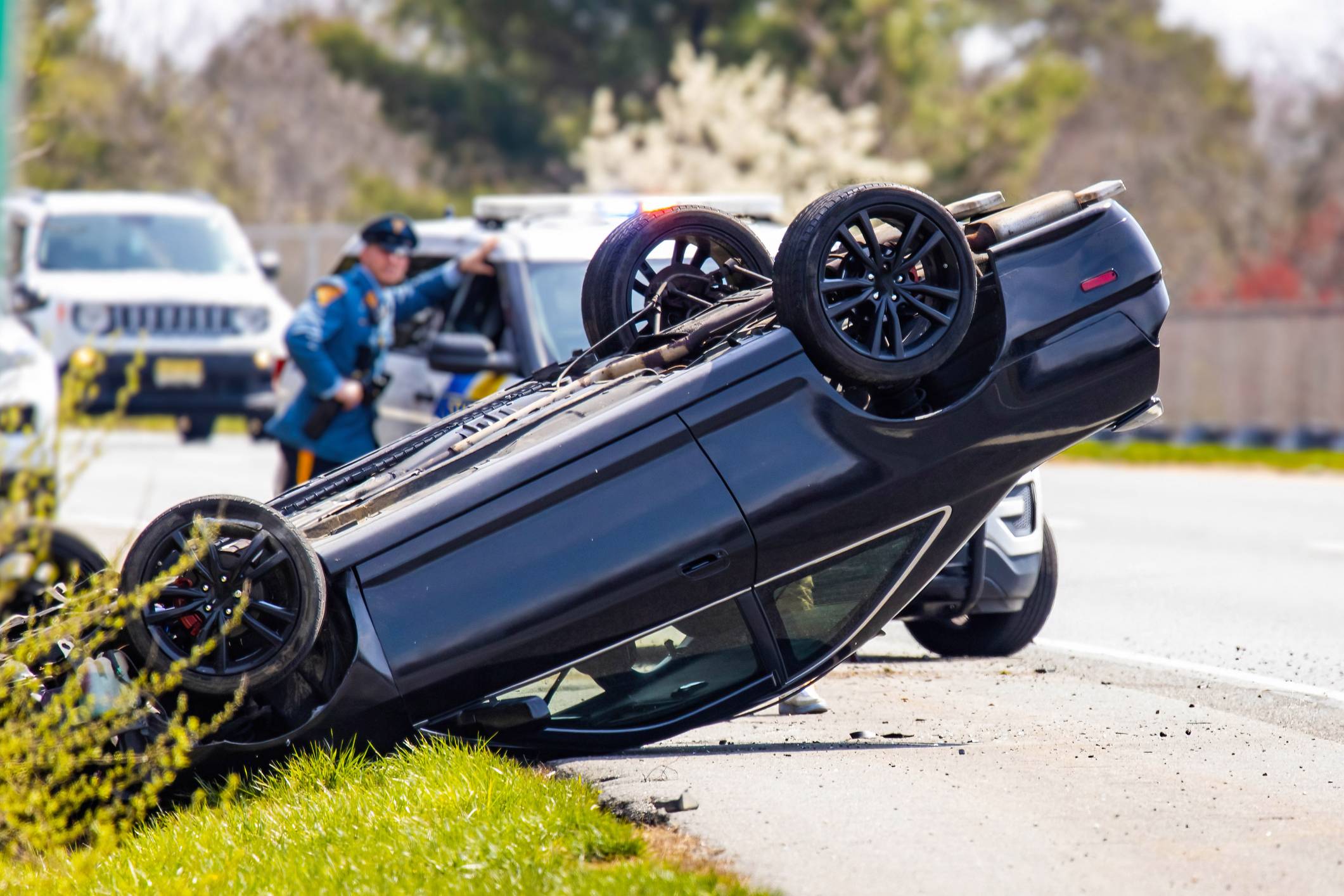 fort lauderdale car accident lawyer - Black car overturned on roadside with police officer and vehicles in background.