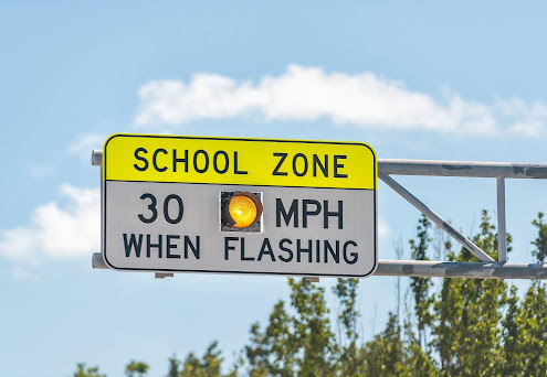 Flashing school zone sign mounted on a metal pole, clear sky in background, text that reads: SCHOOL ZONE 30 MPH WHEN FLASHING. what you should do after an accident in a school zone