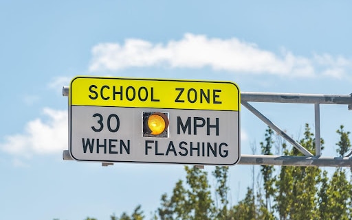 Flashing school zone sign mounted on a metal pole, clear sky in background, text that reads: SCHOOL ZONE 30 MPH WHEN FLASHING. what you should do after an accident in a school zone