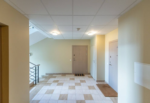 Well-lit apartment hallway with tiled floor, beige walls, and three visible doors, one of which has a striped doormat. when can you sue hoa