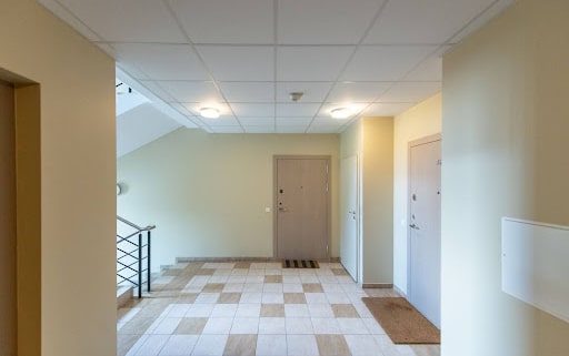 Well-lit apartment hallway with tiled floor, beige walls, and three visible doors, one of which has a striped doormat. when can you sue hoa