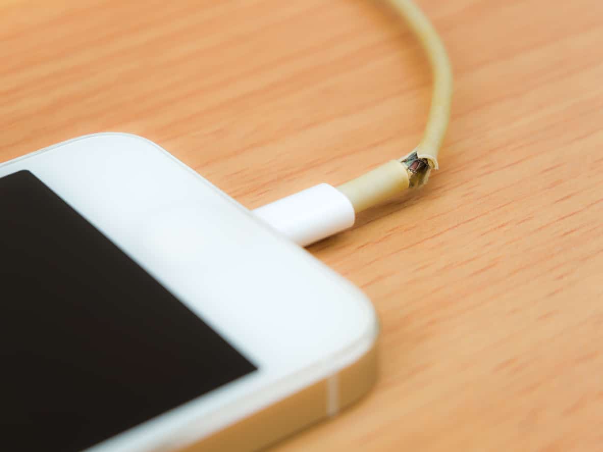 Close of broken charger cable with smart phone on the wooden table