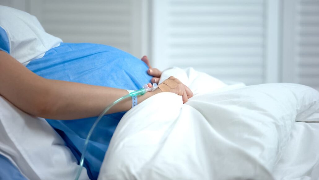 Pregnant woman hospitalized holds her stomach apprehensively.