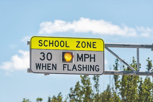 Flashing school zone sign mounted on a metal pole, clear sky in background, text that reads: SCHOOL ZONE 30 MPH WHEN FLASHING. what you should do after an accident in a school zone