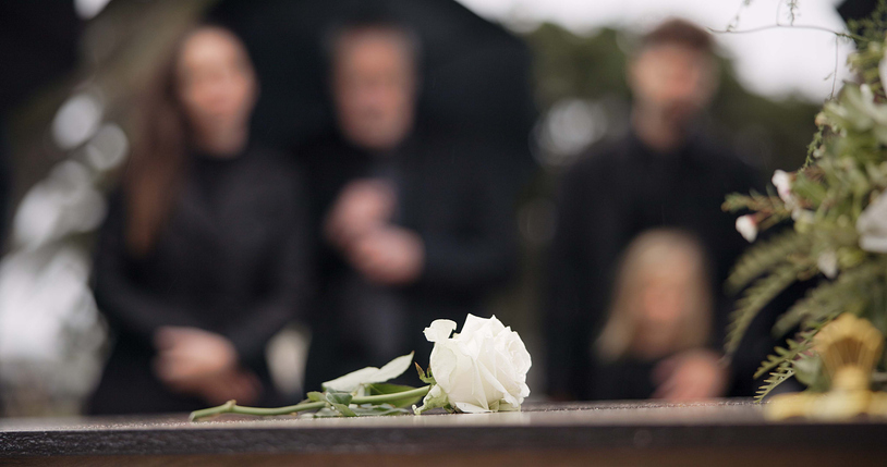 Focus on flower on casket with grieving family in the background - Palm Beach Gardens Wrongful Death Lawyer
