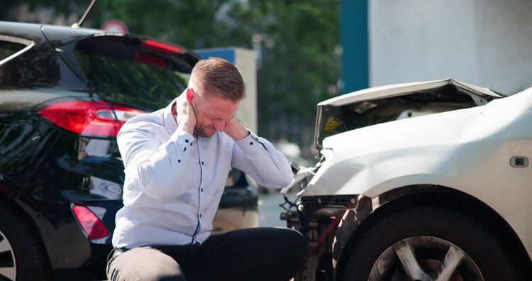 boca raton car accident lawyer - Man kneeling and holding neck in pain beside damaged cars after collision.